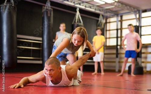 Concentrated preteen girl practicing effective self defence techniques with coach in training room