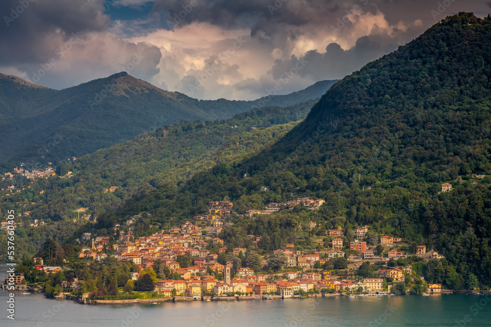 Idyllic Lake Como coastline with village and sailboat at dramatic sunset, Italy