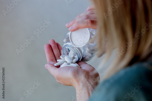 woman pours white pills from a transparent jar into her hand