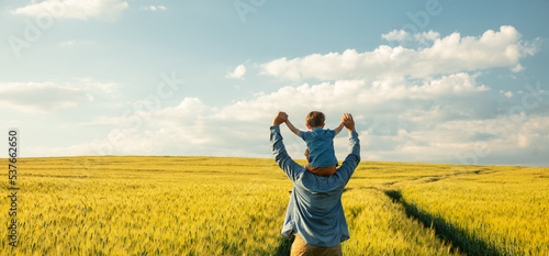 Fotografie father and son in wheat field, child sitting on his fathers shoulders