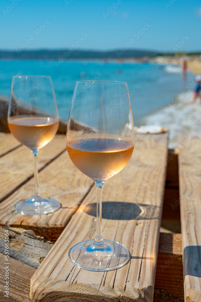 Obraz premium Glasses of cold rose wine from Provence served outdoor on wooden yacht pier with view on blue water and white sandy beach Plage de Pampelonne near Saint-Tropez, France