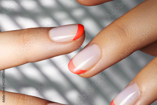 Hands with bright Red French Manicure on Geometric Background. Nails Art Design. Close-up of Female Hands with Trendy Neon Nails on Silver Striped Print Background