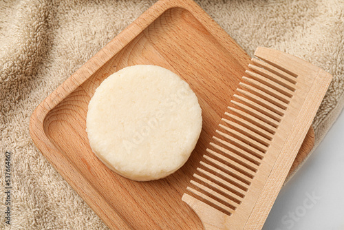 Solid shampoo bar, wooden comb and towel on light table, flat lay