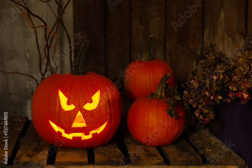 Scary jack o'lantern pumpkin on wooden bench in darkness. Halloween decor