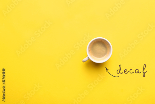 Word Decaf and cup of coffee on yellow background, top view. Space for text