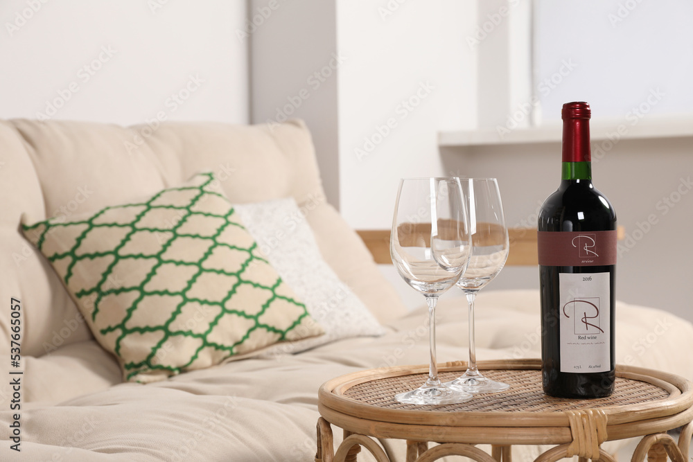 Glasses and wine on rattan table near sofa in living room. Interior design