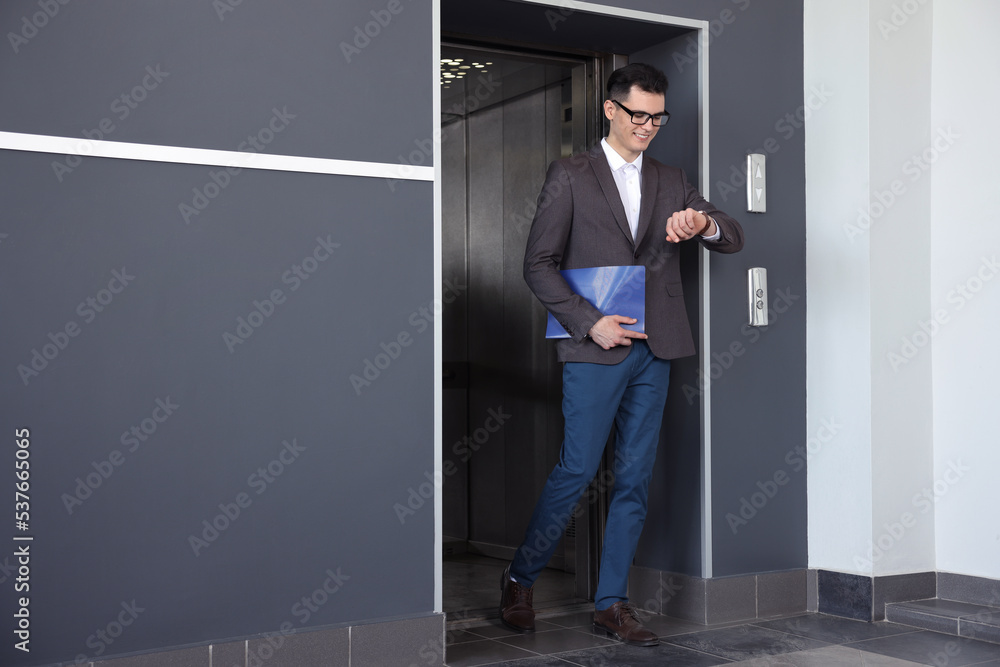 Young businessman walking out of modern elevator Young businessman walking out of modern elevator