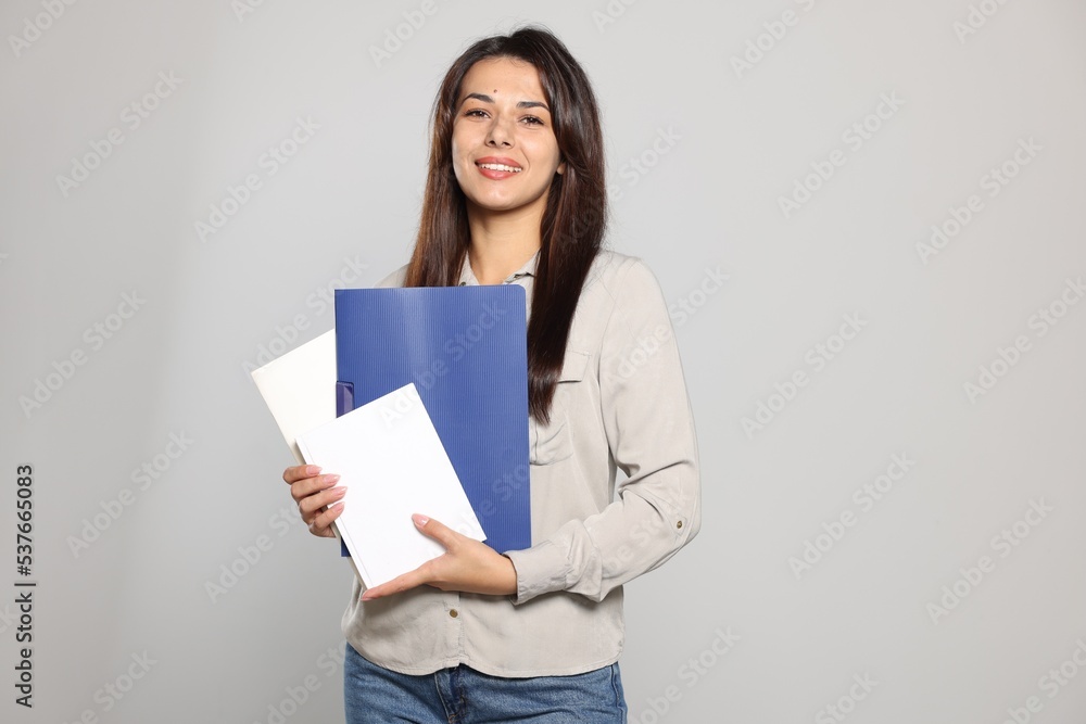 Happy young teacher with books on light grey background. Space for text Happy young teacher with books on light grey background. Space for text