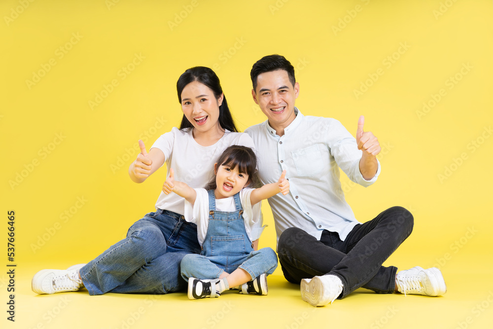 Image of Asian family sitting together happy and isolated on yellow background Image of Asian family sitting together happy and isolated on yellow background