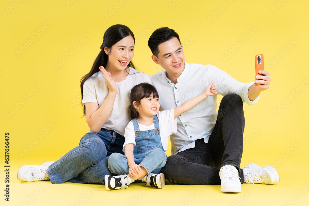 Image of Asian family sitting together happy and isolated on yellow background Image of Asian family sitting together happy and isolated on yellow background
