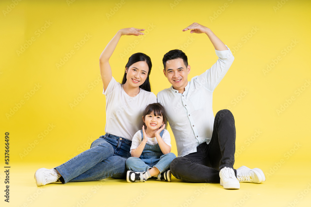 Image of Asian family sitting together happy and isolated on yellow background Image of Asian family sitting together happy and isolated on yellow background