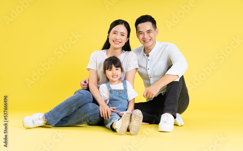 Image of Asian family sitting together happy and isolated on yellow background
