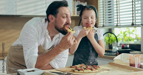 Wallpaper Mural Young delighted father with adorable pretty preschooler daughter in modern kitchen at home standing at table tasting delicious homemade domestic pizza. Charming in good mood girl spending time. Torontodigital.ca