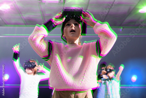 Surprised tween girl wearing VR headset playing virtual reality games in special room. Toned image with stereoscopic anaglyph effect photo