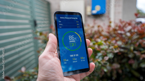 A man checks the charging status of a home installed battery storage unit on a smartphone.