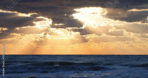 Ocean beach sunrise with dark sky clouds and sun rays over sea waves