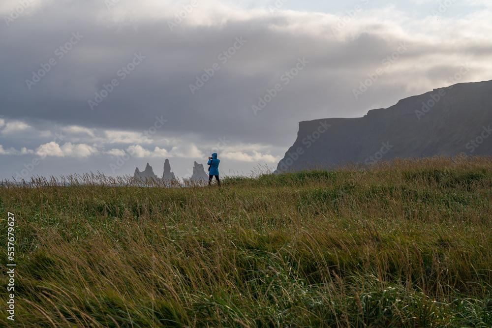 person in jacket taking pictures in winter of mountains and sea from a meadow during a thunderstorm