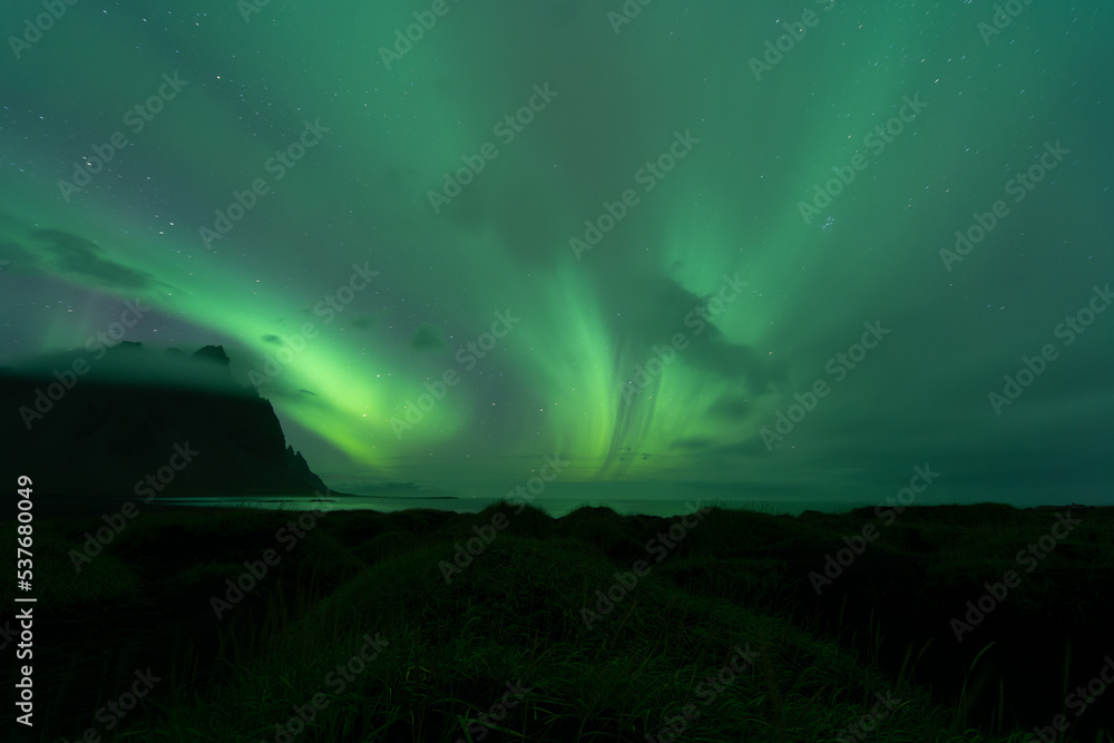 Northern lights over the sea in Iceland. Night on a beach of black volcanic sand and vegetation.