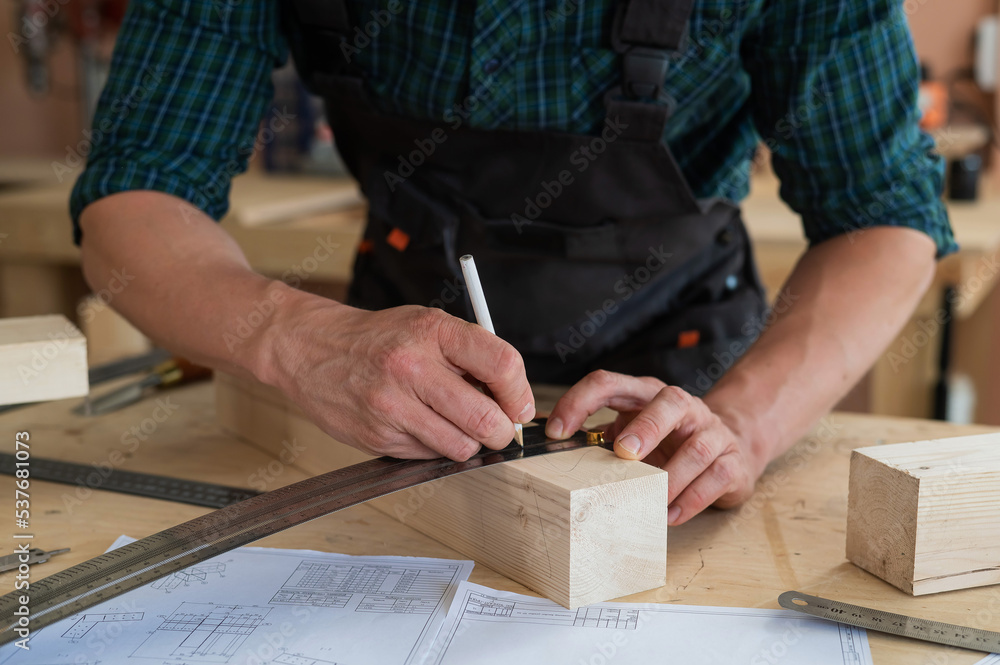 A carpenter measures wooden planks and makes marks with a pencil in a workshop. A carpenter measures wooden planks and makes marks with a pencil in a workshop.