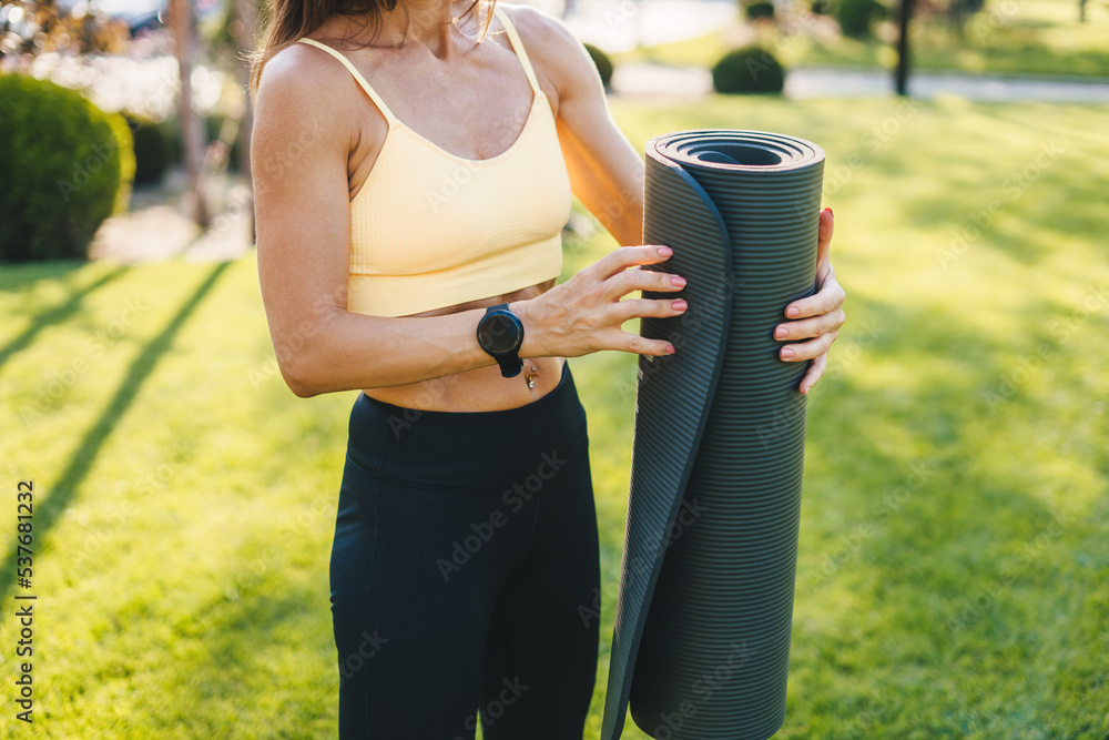 Female hands unrolling yoga mat before workout exercise in the park. Fitness workout. Fitness woman. Young active woman. Nature concept. Healthy lifestyle