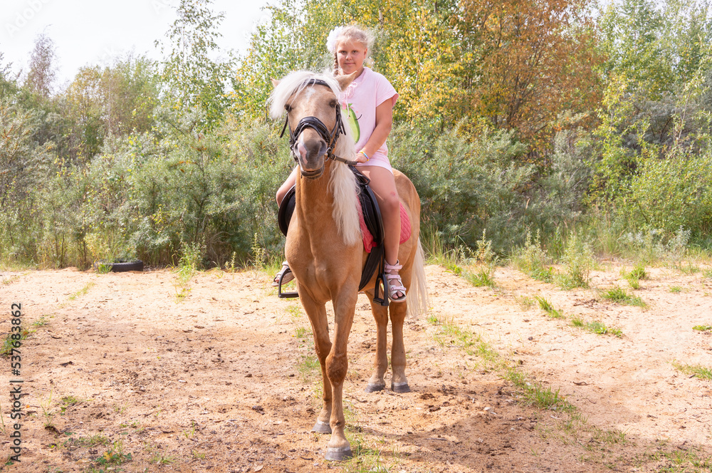 Outside on a beautiful warm day, a girl rides a horse.