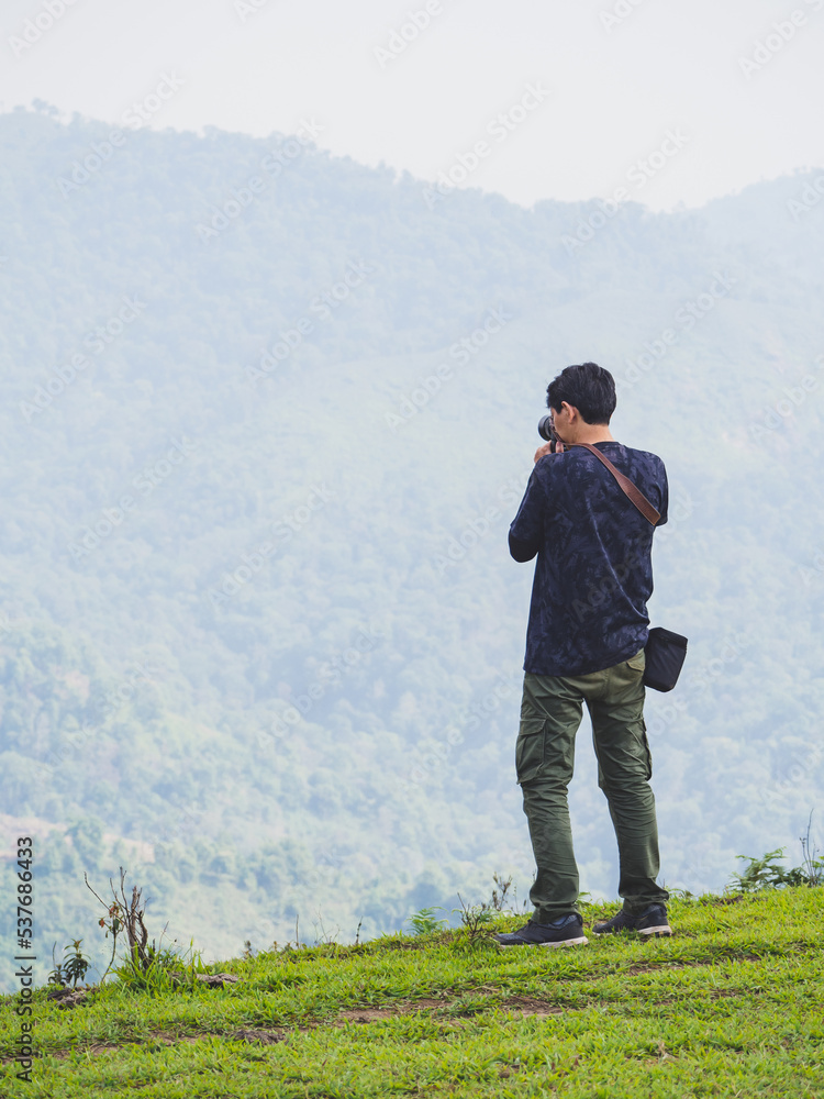 Man hiker with backpack standing on top of the mountain and taking picture of valley Man hiker with backpack standing on top of the mountain and taking picture of valley