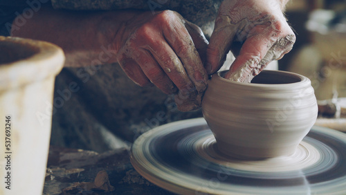 Work in pottery workshop: clay ware on throwing wheel, master ceramist molding clay using professional tools. Creating ceramic utensils and traditional occupation concept. photo