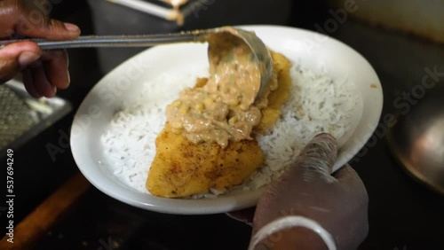 Chef ladels maque choux cream corn sauce over pan fried catfish on a bed of white rice, slow motion 4K photo