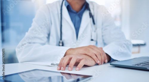 Hands  tablet and healthcare with a doctor at a desk in the hospital for medicine  insurance or consulting. Trust  medical and internet with a male surgeon sitting in a clinic for health or wellness