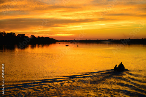 The silhouette of a small motorized canoe against a golden dusk on the Guaporé - Itenez river, Ricardo Franco village, Vale do Guaporé Indigenous Land, Rondonia, Brazil, on the border with Bolivia photo