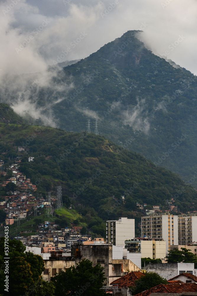 The cloud-shrouded Andaraí Maior peak and the Atlantic rainforest of Tijuca National Park towering above favelas and neighboring districts of the Zona Norte, or North Zone of Rio de Janeiro, Brazil
