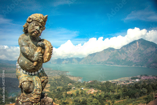 A small statue on a hill with a lake and mountains in the background in bali