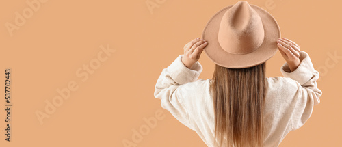 Beautiful fashionable young woman on beige background with space for text, back view