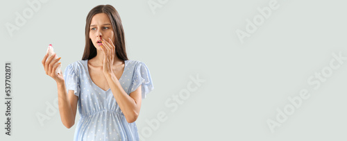 Young pregnant woman with nosebleed and tissue on light background with space for text