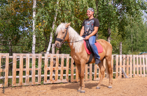 Outside on a beautiful warm day, a young man is riding a horse.