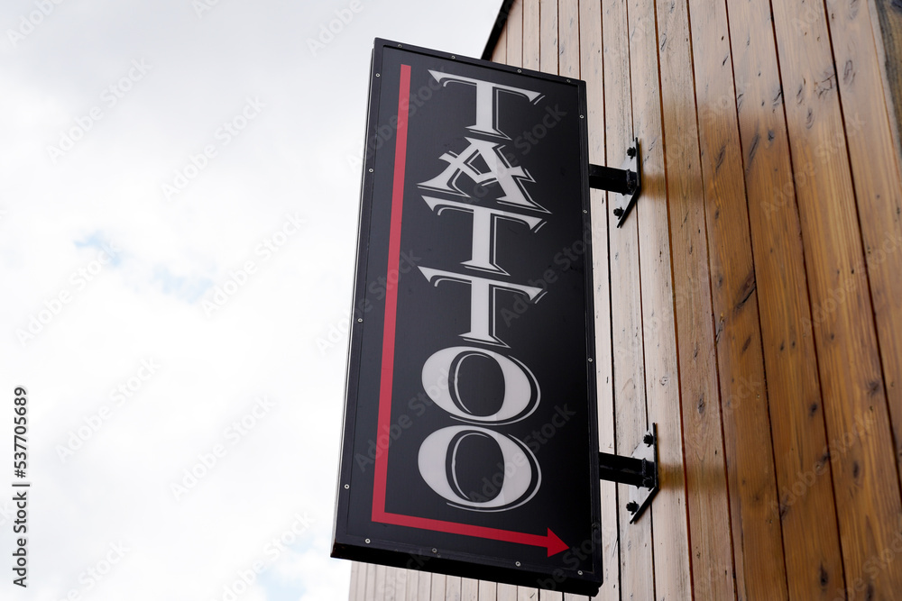 Tattoo text sign in letters white on facade wall shop entrance in the city street Tattoo text sign in letters white on facade wall shop entrance in the city street