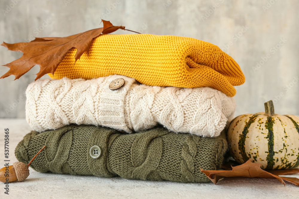Stack of different children's sweaters and autumn decor on light background