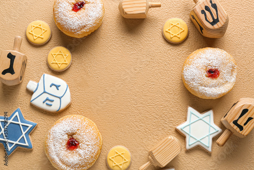 Frame made of wooden dreidels, cookies and donuts for Hanukkah celebration on color background
