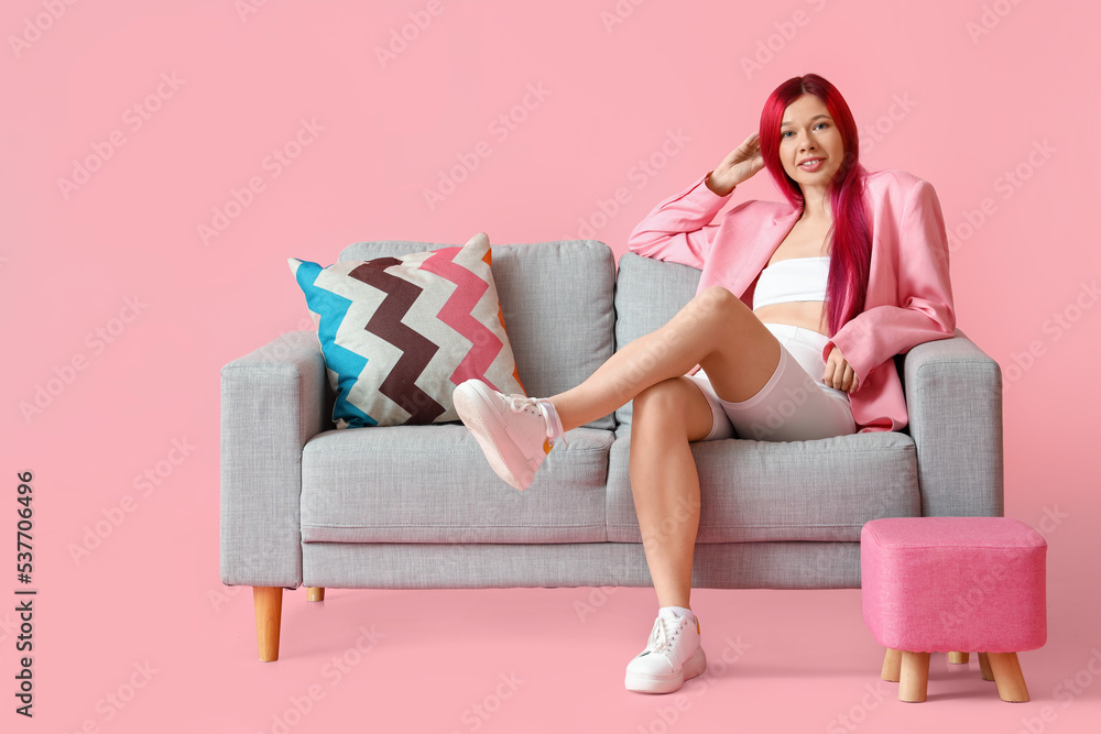 Pretty young woman with unusual hair relaxing on sofa against pink background Pretty young woman with unusual hair relaxing on sofa against pink background