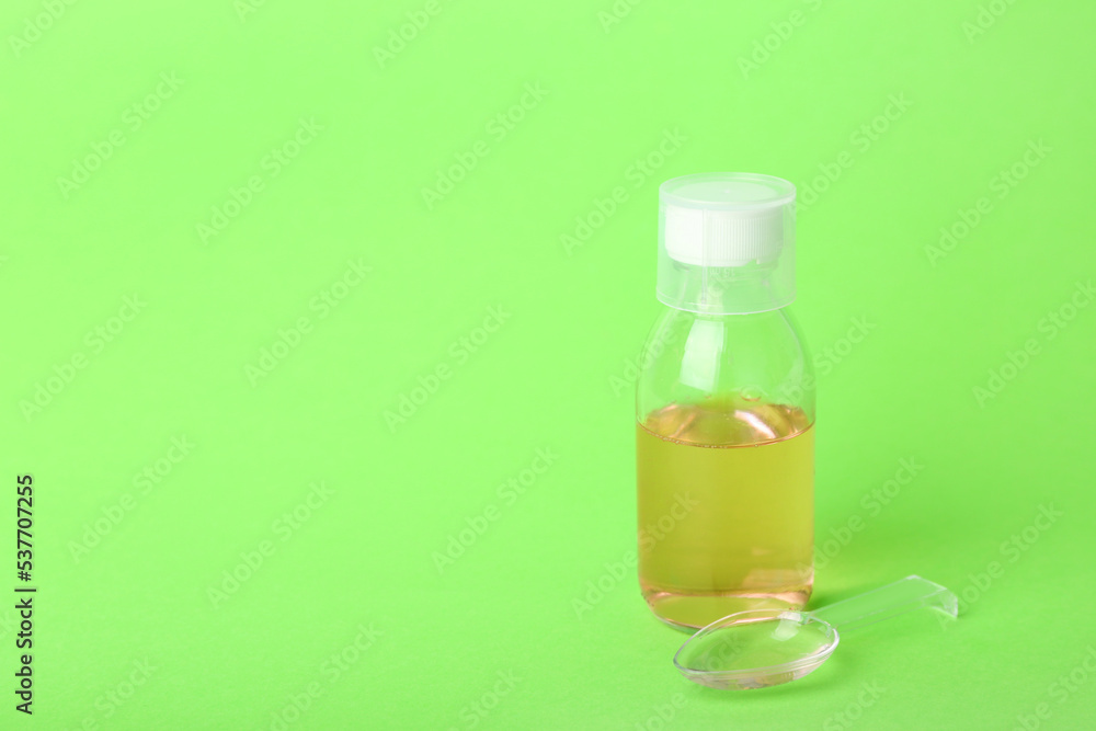 Bottle and spoon of cough syrup on green background Bottle and spoon of cough syrup on green background