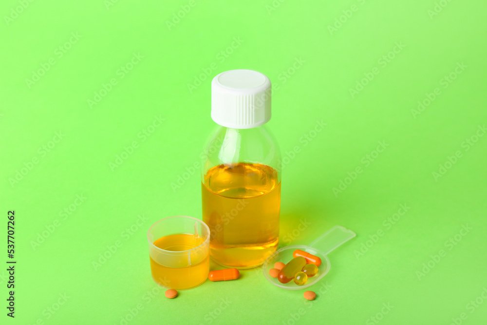 Bottle of cough syrup, cup and pills on green background Bottle of cough syrup, cup and pills on green background