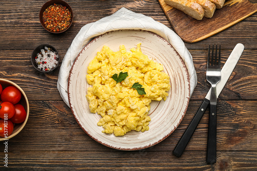 Plate of tasty scrambled eggs, tomatoes and spices on wooden background