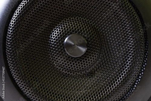 The central fragment of a modern audio speaker with a protective black metal grille. Macro.