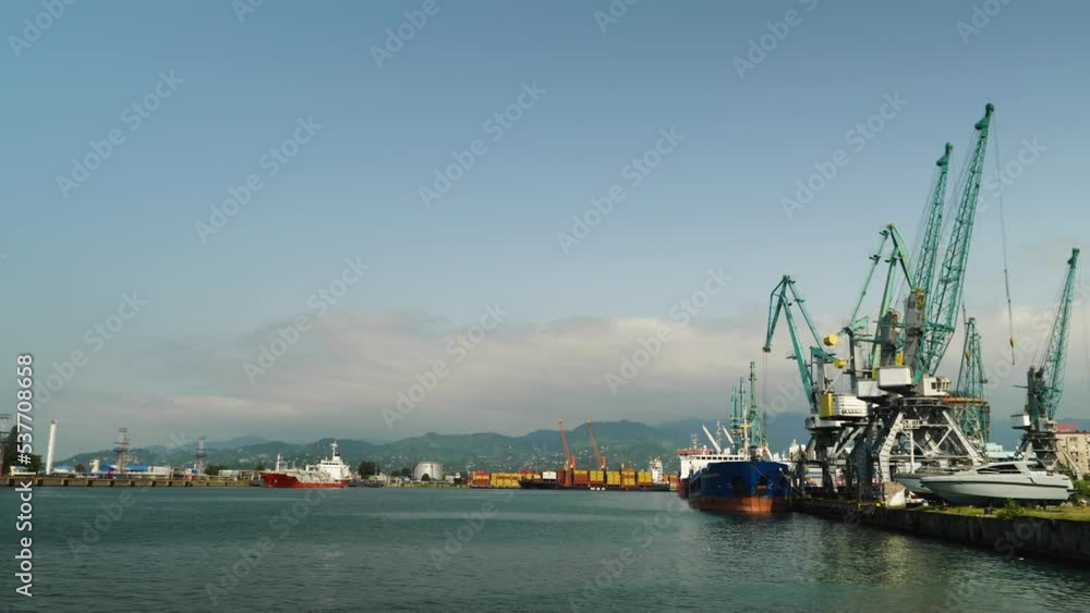 Heavy equipment cranes at the seaport. Concept of industry and transport. Export and import of dry cargo by sea around the world. In the background a vessel with LNG and containers Heavy equipment cranes at the seaport. Concept of industry and transport. Export and import of dry cargo by sea around the world. In the background a vessel with LNG and containers