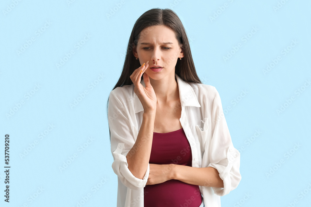 Young pregnant woman with nosebleed on blue background Young pregnant woman with nosebleed on blue background