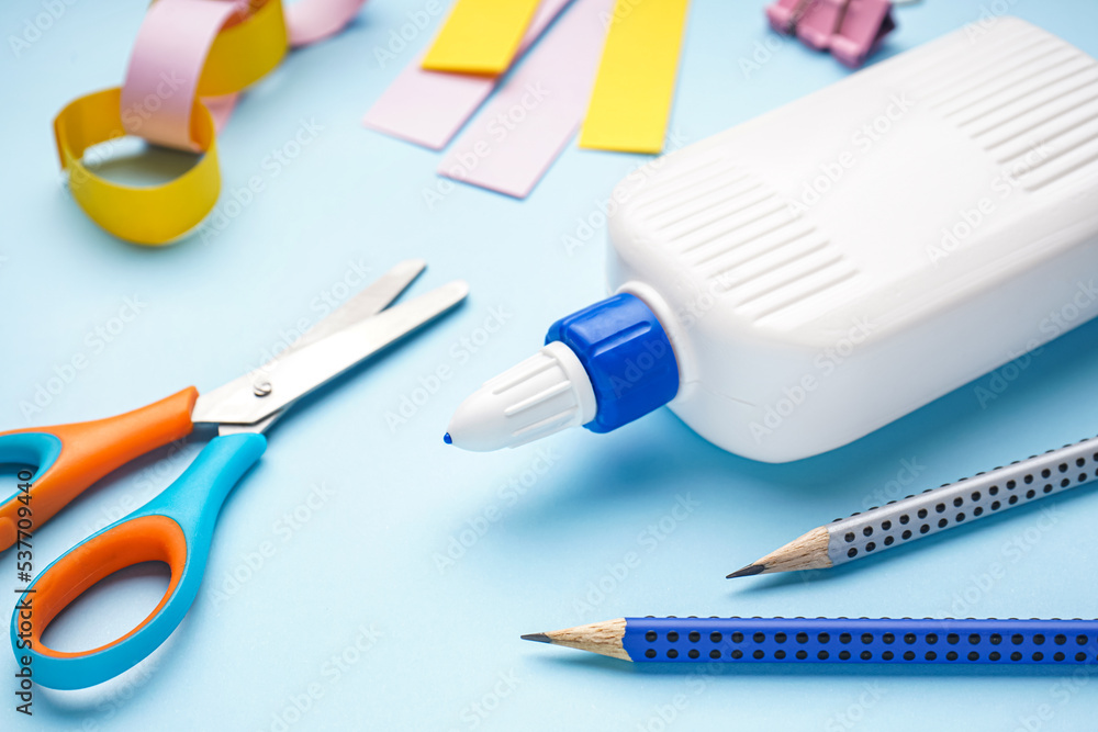 Bottle of glue with pencils and scissors on blue background, closeup Bottle of glue with pencils and scissors on blue background, closeup