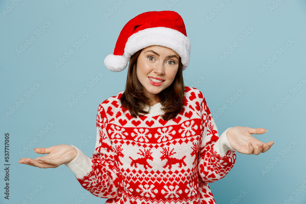 Young woman 20s wear warm red knitted sweater Santa hat posing shrugging shoulders looking puzzled spread hands isolated on plain pastel light blue cyan background Happy New Year 2023 holiday concept Young woman 20s wear warm red knitted sweater Santa hat posing shrugging shoulders looking puzzled spread hands isolated on plain pastel light blue cyan background Happy New Year 2023 holiday concept