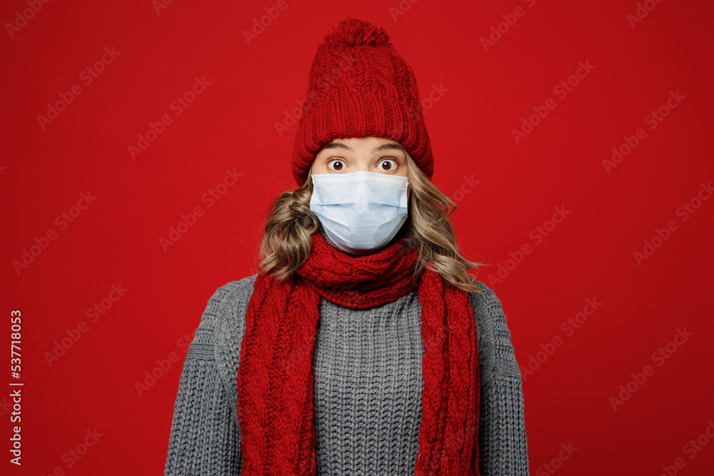 Young pop-eyed woman in grey sweater scarf hat sterile mask save from coronavirus look camera isolated on plain red background studio Healthy lifestyle ill sick disease treatment cold season concept Young pop-eyed woman in grey sweater scarf hat sterile mask save from coronavirus look camera isolated on plain red background studio Healthy lifestyle ill sick disease treatment cold season concept