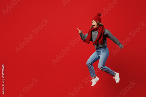 Full body side view young woman wear grey sweater scarf hat jump high run hurry up isolated on plain red background studio portrait. Healthy lifestyle ill sick disease treatment cold season concept.
