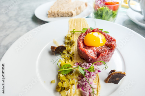 Traditional beef tartar served with a raw egg on top, onion and cucumber in white plate ready to be eaten